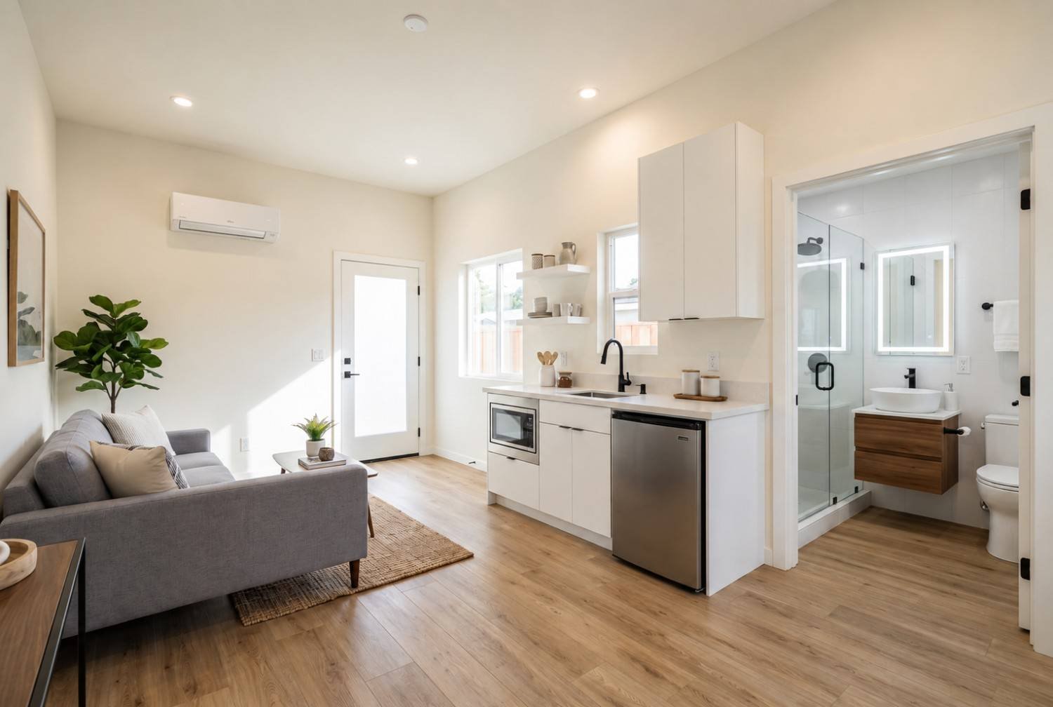 Modern ADU interior with an open living area, compact white kitchen, mini-split HVAC, luxury vinyl flooring, and a contemporary bathroom with a glass walk-in shower.