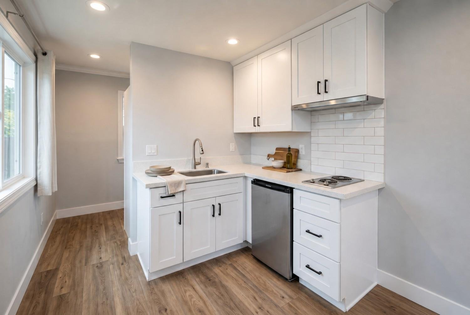 Compact modern ADU kitchen with white shaker cabinets, quartz countertops, subway tile backsplash, stainless steel appliances, and wood-look vinyl flooring.